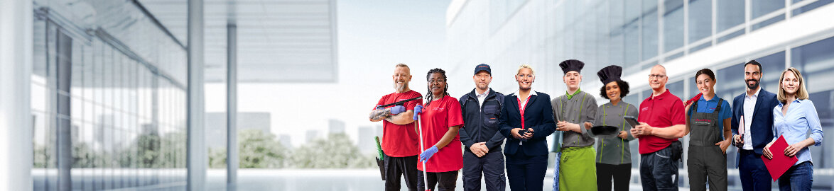 Photo de groupe d'employés souriants de Dussmann issus de différents domaines professionnels, devant un fond gris neutre