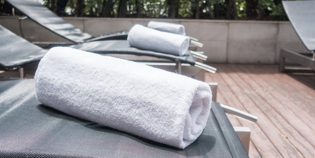 Service de blanchisserie Dussmann pour les espaces bien-être, fournissant du linge doux, propre et hygiénique, adapté aux besoins des spas, centres de bien-être et hôtels, tout en respectant des protocoles stricts d'hygiène et de qualité | © <a href="https://www.freepik.com/free-photo/white-towels-deck-chairs_952848.htm">Image by mrsiraphol on Freepik</a>
